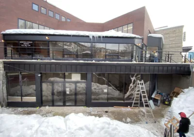 Modern building under construction during winter, featuring large windows and a balcony with icicles hanging from the roof.