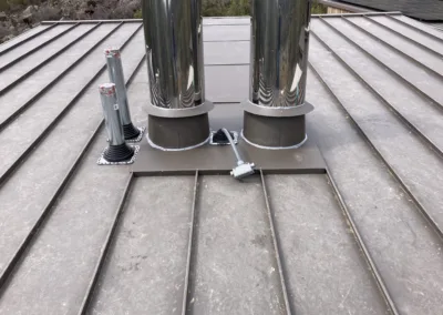 Two cylindrical metal ventilation ducts installed on a metal roof with external wiring and control units.