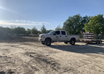 A pickup truck hauling materials in a dirt lot with trees in the background.