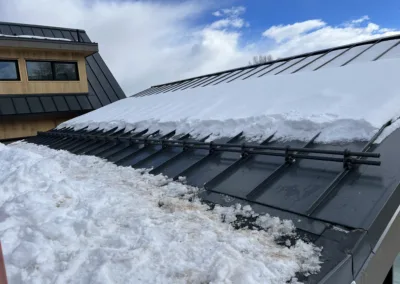 Snow-covered metal roof with solar panels and a clear blue sky.