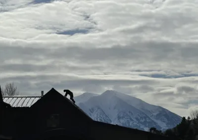 Silhouetted figure working on a rooftop against a backdrop of mountains and overcast skies.