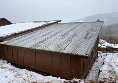 A metal-roofed building with snow partially covering the roof and surrounding ground.