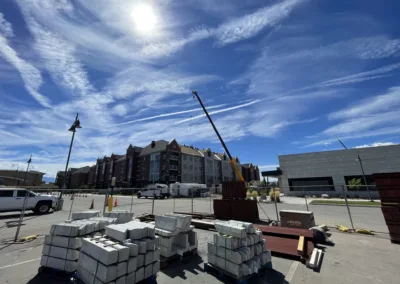 Construction materials in the foreground with a crane and building under construction under a clear blue sky.