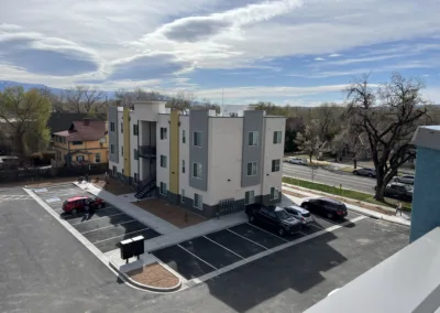 Newly constructed modern apartment building with an adjacent parking lot, surrounded by mature trees under a clear sky.