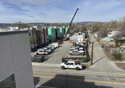 Construction site with a crane next to a partially completed building, surrounded by parked vehicles and with distant mountains in the background.