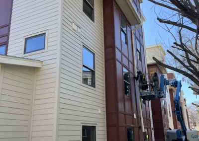 Two workers on a blue lift conducting maintenance or repairs on a multi-story building with white and brown siding.