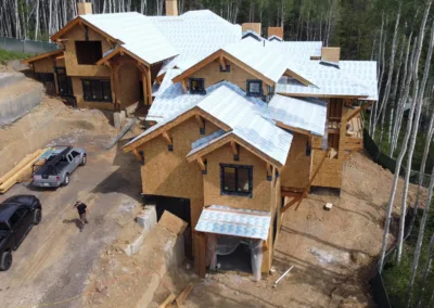 Aerial view of a large residential construction site with unfinished wooden structures and roofing, featuring workers and vehicles present on site.